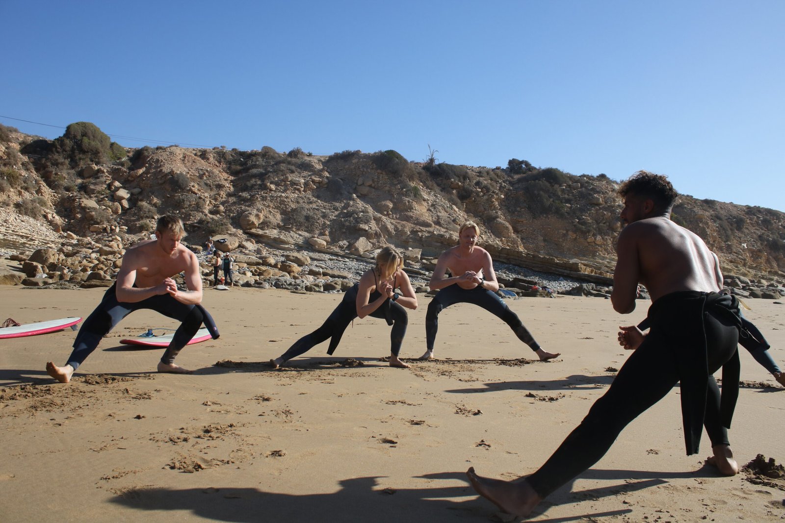 Surfers warming up on the beach in Morocco before catching waves – stretching exercises under the morning sun by the ocean.